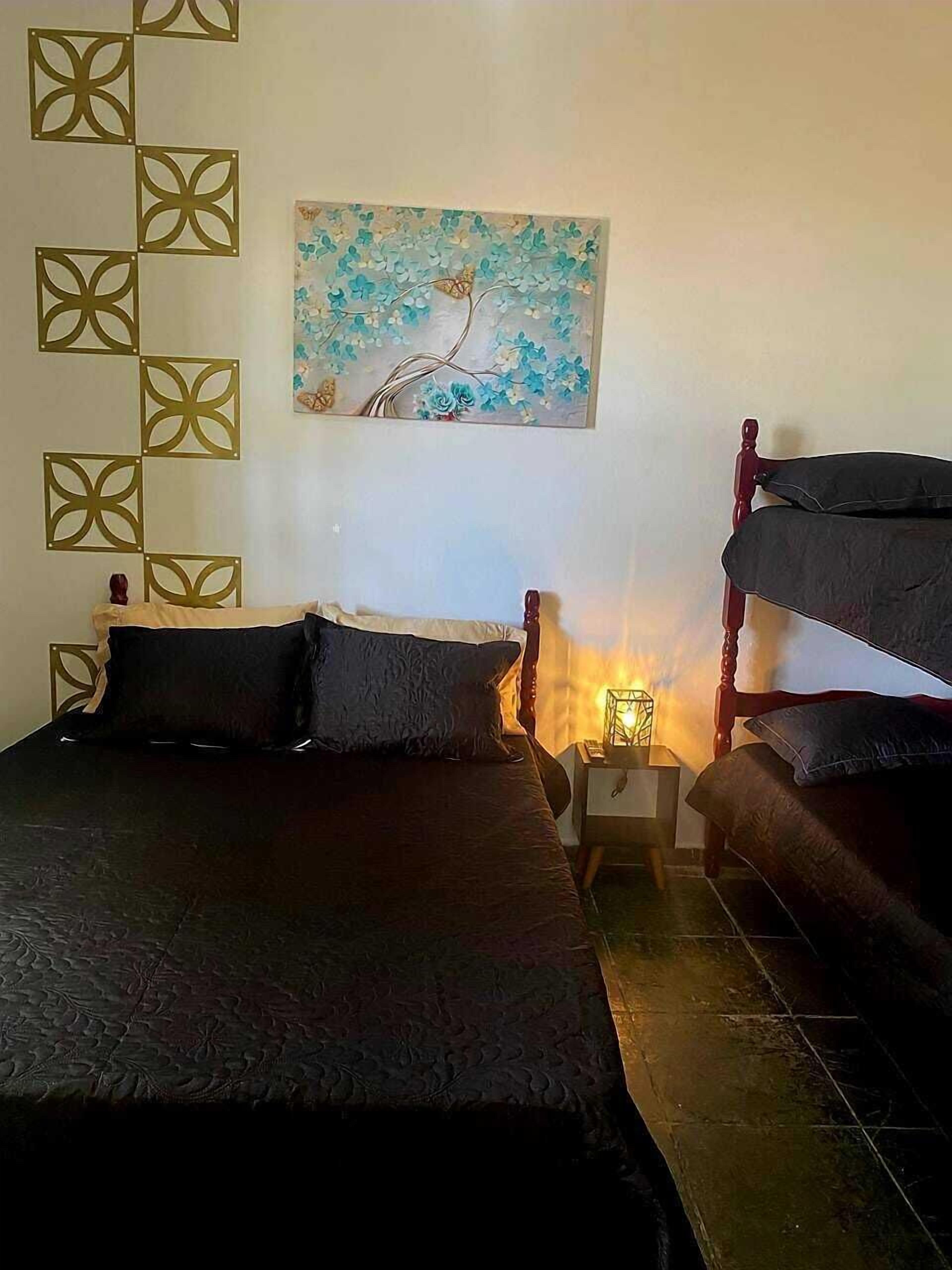 A bedroom with a bed, a nightstand, a lamp, a painting, and a geometric wall decoration.