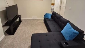 Een woonkamer met een zwarte bank, een zwart voetenbankje en een flatscreen televisie op een standaard.