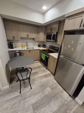 Una cocina compacta con armarios de madera, un refrigerador de acero inoxidable, un microondas y una estufa.