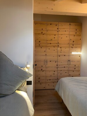 Une chambre avec une armoire en bois, un lit avec une literie à rayures et une lampe sur le côté gauche.