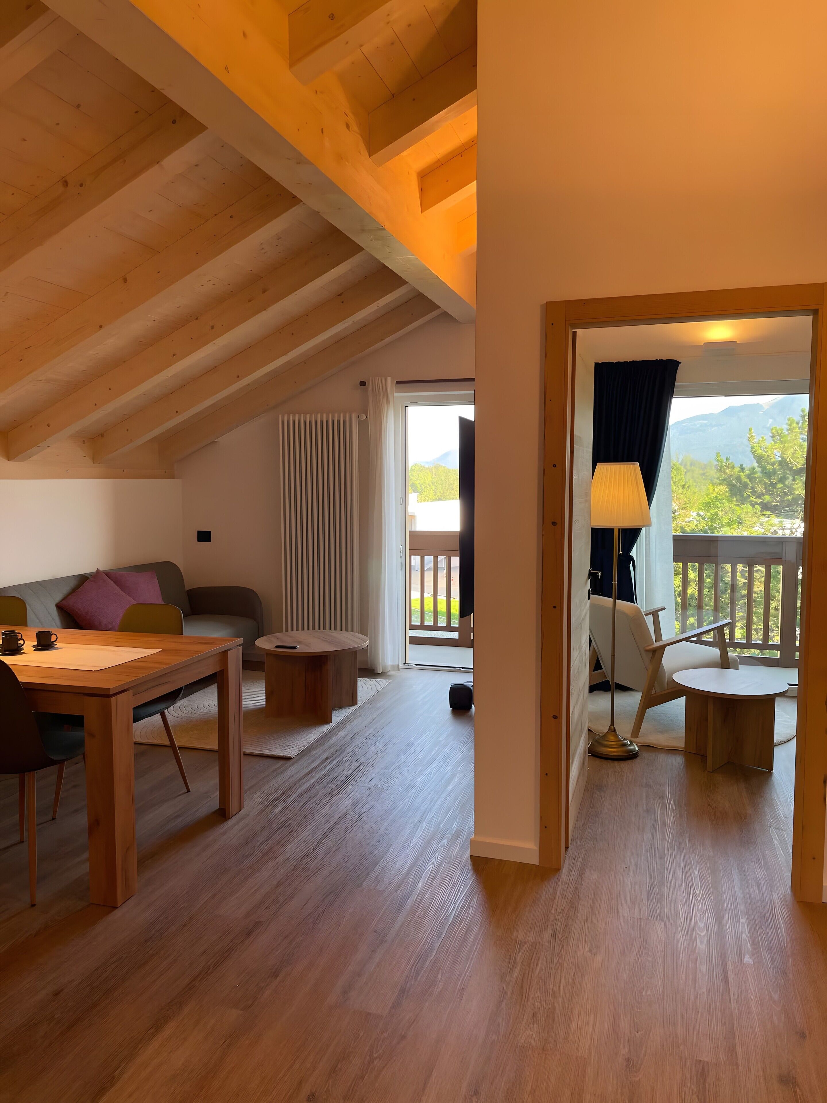 Un loft espacioso con techos altos, vigas de madera, zona de comedor, sofá, balcón con vistas y puerta corredera que da a un espacio exterior.
