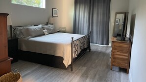 Une chambre à coucher avec un lit, des tables de chevet, une commode, une fenêtre et un rideau.
