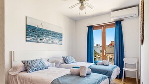 A hotel room with two beds, a ceiling fan, a window with curtains, and a view of the sea.
