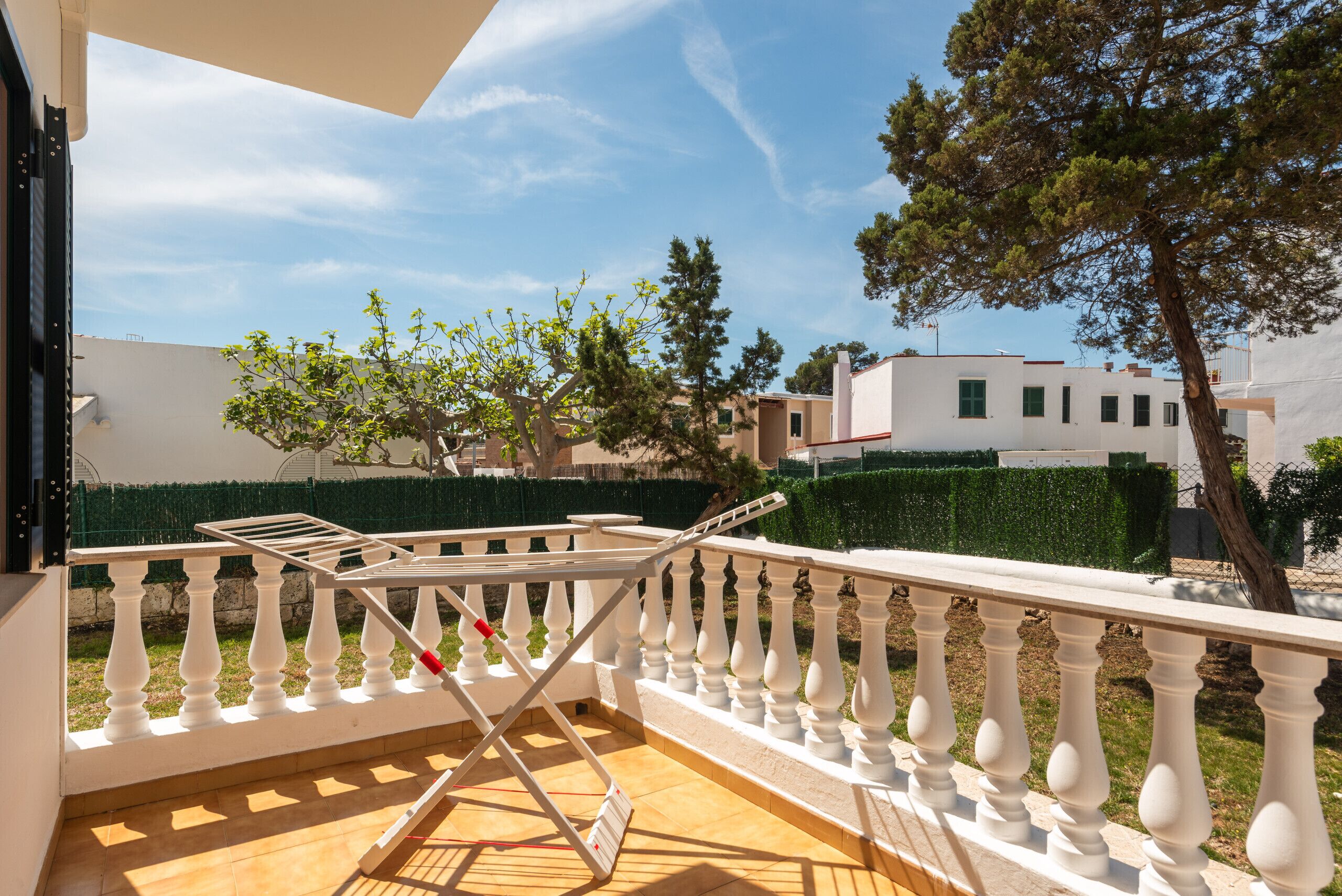 Een balkon met een witte balustrade, een droogrek en uitzicht op omliggende gebouwen en bomen.
