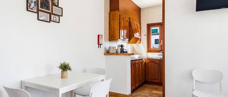 Eine moderne Küche mit Holzausstattung, einem weißen Esstisch mit Stühlen und einem an der Wand befestigten Flachbildfernseher.
