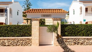 A gated entrance with a sign reading 'Apartamentos Mar Blanca,' surrounded by stone walls and a palm tree.