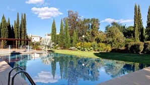 A swimming pool with a clear reflection, surrounded by trees and a well-maintained lawn. - Villa Soligolf - Vilamoura, Algarve (Villamoura)
