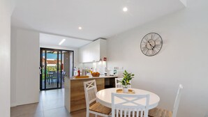 A modern kitchen with white cabinets, a dining table with white chairs, and a wall clock. - Villa Soligolf - Vilamoura, Algarve (Villamoura)