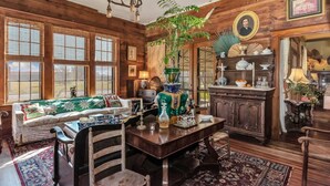 Een klassieke kamer met houten wanden, een bank, een eettafel met stoelen, een kroonluchter en een grote plant.