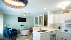 A modern kitchen with white cabinetry, a built-in microwave, and a stainless steel stove. There is a dining area with a round table and chairs, and a blue sofa. - AK Getaway Too ,where the waves kiss the shore and worries melt away. (Port Aransas)
