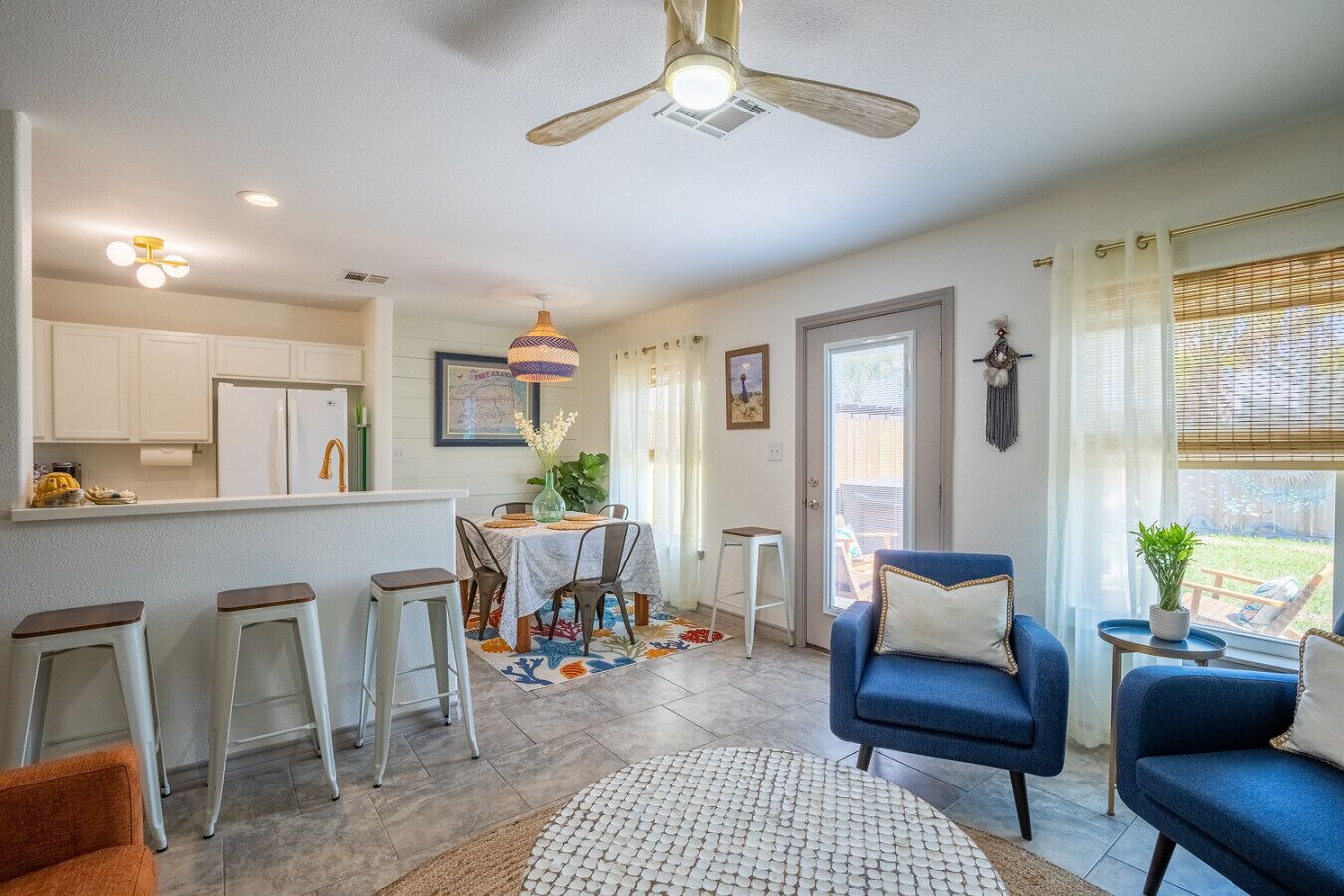 A modern kitchen with white cabinets, a dining area with a table and chairs, a blue sofa, and a ceiling fan.