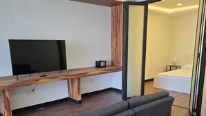 Un soggiorno moderno con televisore piatto, mobile TV in legno, divano grigio e un tavolino con lampada.
