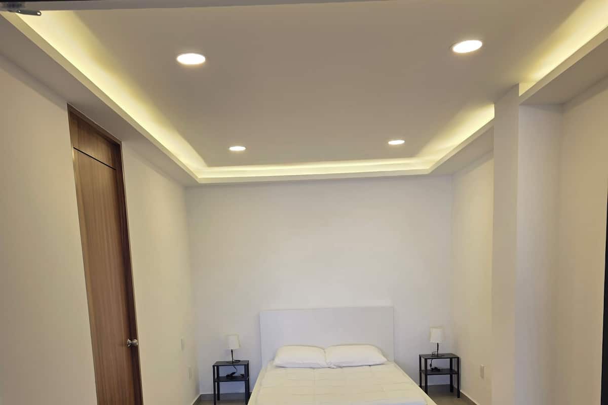 Een slaapkamer met een bed, twee nachtkastjes, een houten deur en inbouwspots.