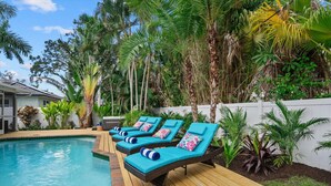 Un área junto a la piscina con sillones de descanso y una terraza de madera.