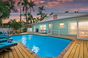 A swimming pool with lounge chairs, a barbecue area, and a view of palm trees.