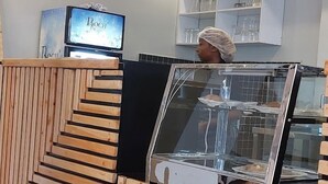 Eine Theke in einer Bäckerei, gestaltet mit Holzlamellen, eine Glasvitrine und ein Bildschirm, der 'Bock' anzeigt.