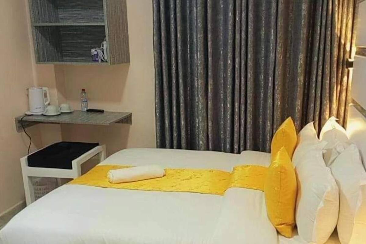 Una habitación de hotel con una cama, una mesita de noche con una tetera, una botella de agua y una taza.