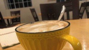 Eine gelbe Tasse mit Löffel auf einem Holztisch.