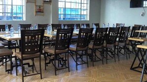 Ein Konferenzraum mit mehreren Tischen und Stühlen, großen Fenstern und einer Deckenleuchte.