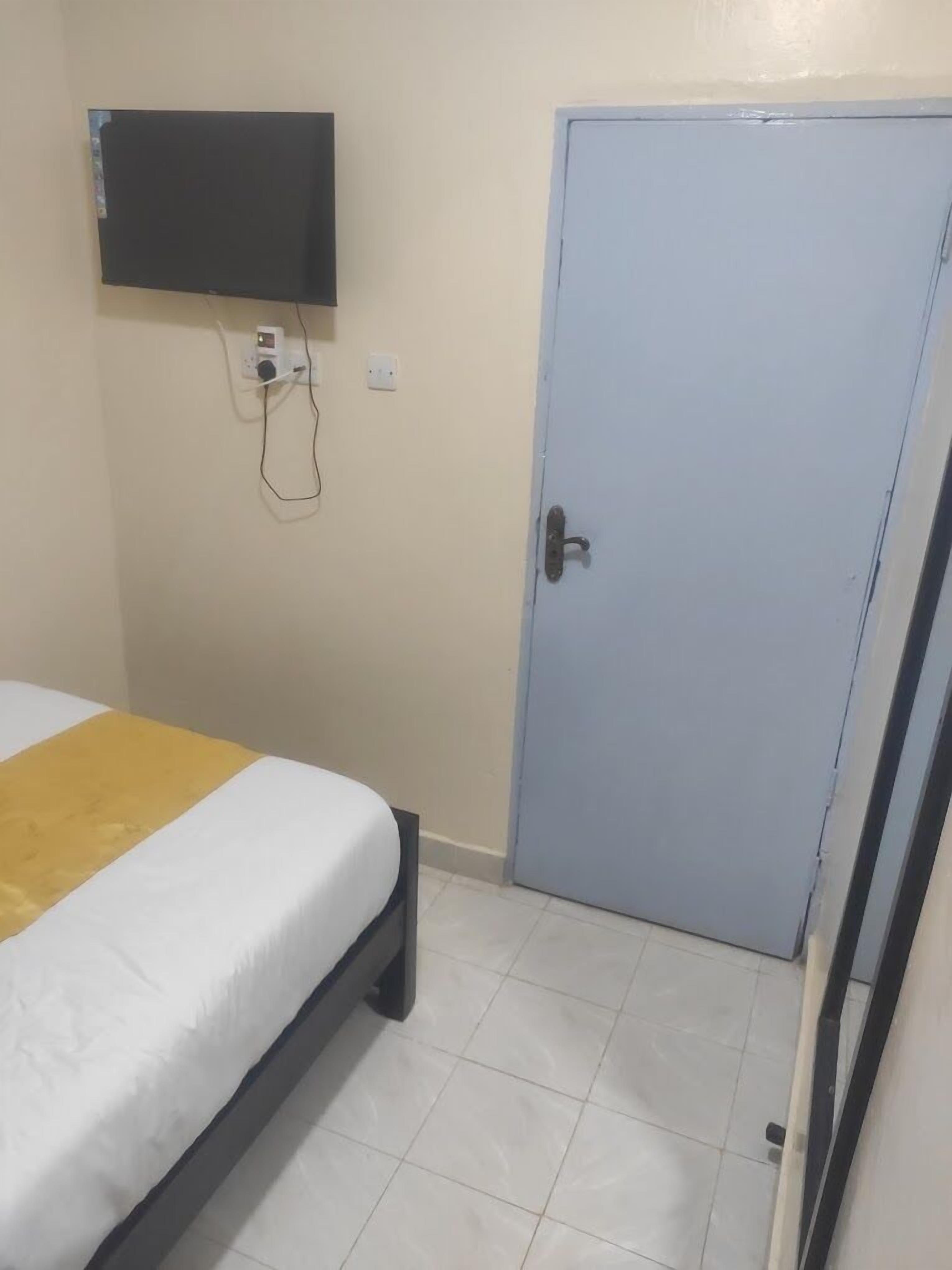Un lit simple agrémenté d’une touche de jaune, une porte fermée et un téléviseur fixé au mur.