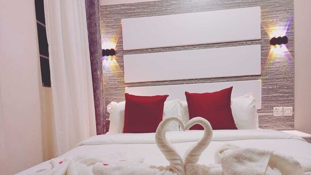 Ein Hotelzimmer mit einem ordentlich bezogenen Bett, einer herzförmigen Handtuchgestaltung und einem roten Kopfkissen.