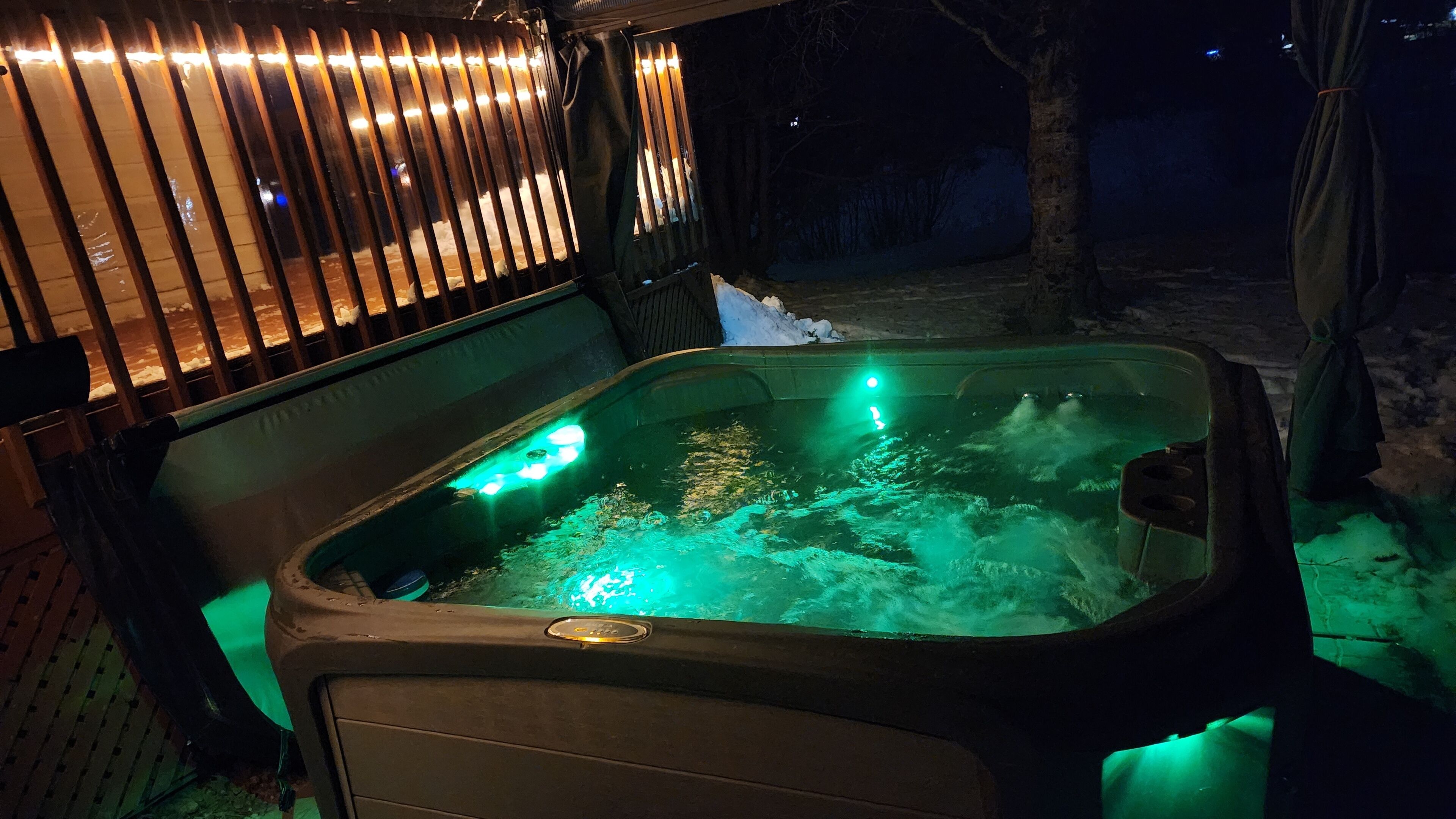 Ein Whirlpool mit grüner Beleuchtung, umgeben von einem Holenzaun und Schnee.