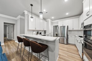 A modern kitchen with white cabinetry, stainless steel appliances, and a central island with bar stools. - Woodland Retreat at Chapel Hill (Chapel Hill)