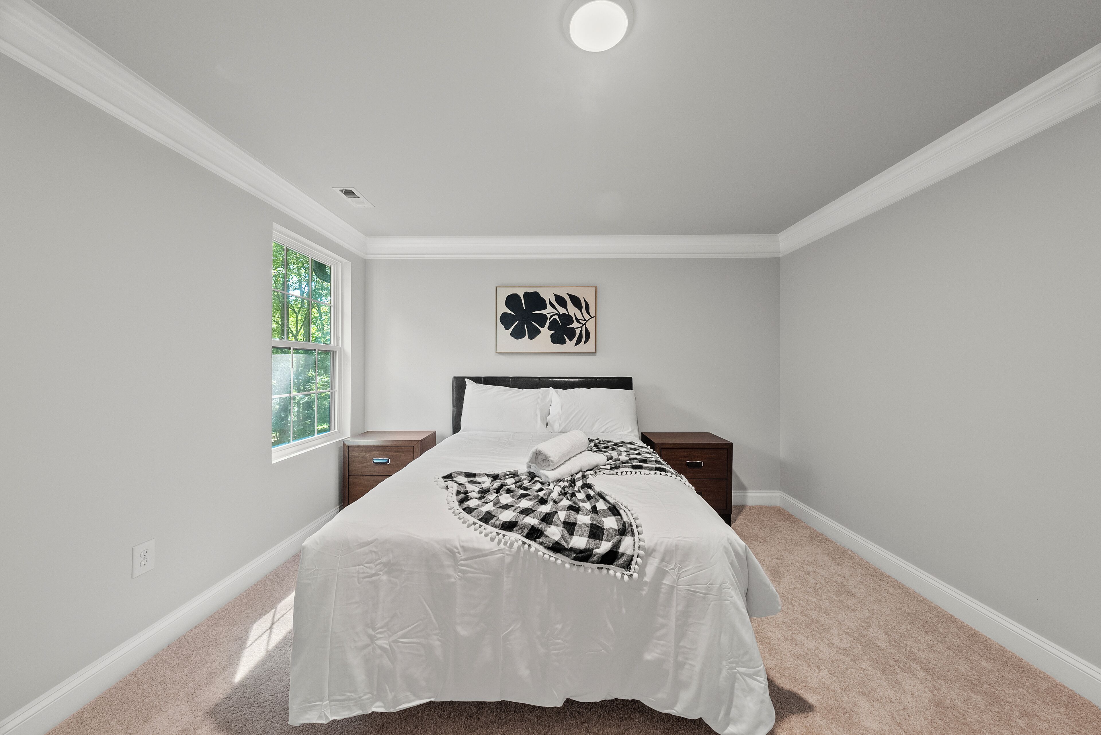 Une chambre à coucher comprenant un lit, une fenêtre, une table de chevet et une œuvre d’art accrochée au mur.