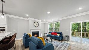A modern living room with a fireplace, blue sofas, and a dining area with bar stools. - Woodland Retreat at Chapel Hill (Chapel Hill)