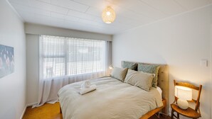 Een slaapkamer met een bed, een raam met zonwering, een lamp en een stoel.
