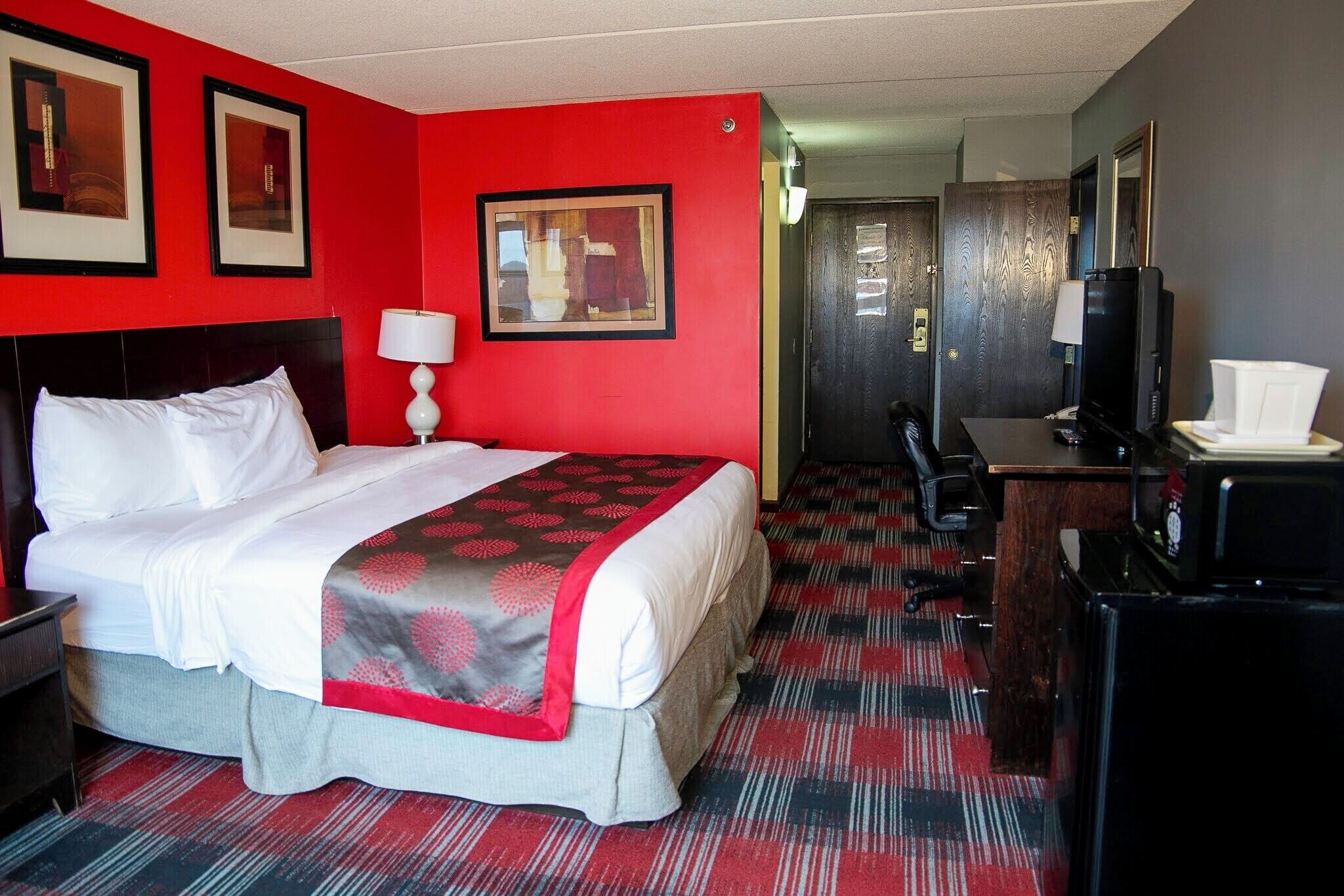 Een hotelkamer met een groot bed, een bureau met een computer, een televisie en een rode muur.
