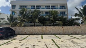 A modern building with a white facade and blue accents, surrounded by palm trees and a parking area. - Comfortable and modern studio (Punta Cana)
