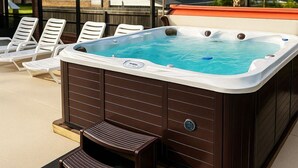 Ein Whirlpool mit Holzverkleidung, einem Einstieg und weißen Liegestühlen im Hintergrund.