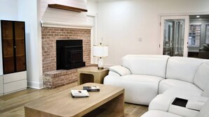 Ein modernes Wohnzimmer mit Kamin aus Backstein, einer weißen Ledersofa und einem Holztisch.