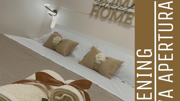 A hotel room with a neatly made bed, a wall sign that reads "HOME HOME," and a sign indicating a new opening. - Sweet House Miracles (Napoli)