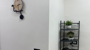 A corner of a room with a wall-mounted clock and a black metal shelf unit with plants. - Sweet House Miracles (Napoli)