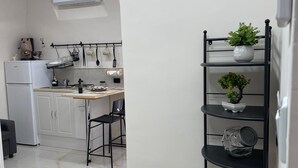 A modern kitchen with white cabinets, a black metal chair, and a black metal shelf with plants. - Sweet House Miracles (Napoli)