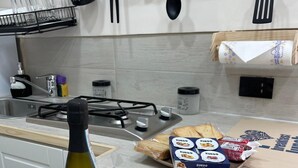 A kitchen with a gas stove, a bottle of wine, a glass, a tray of bread, and a breakfast mat. - Sweet House Miracles (Napoli)