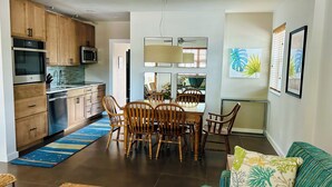A modern kitchen with wooden cabinets and stainless steel appliances, a dining area with a wooden table and chairs, and a living room with a sofa and a coffee table. - Serendipity South: Premium Key West Pool Oasis Near The Beach (Key West)