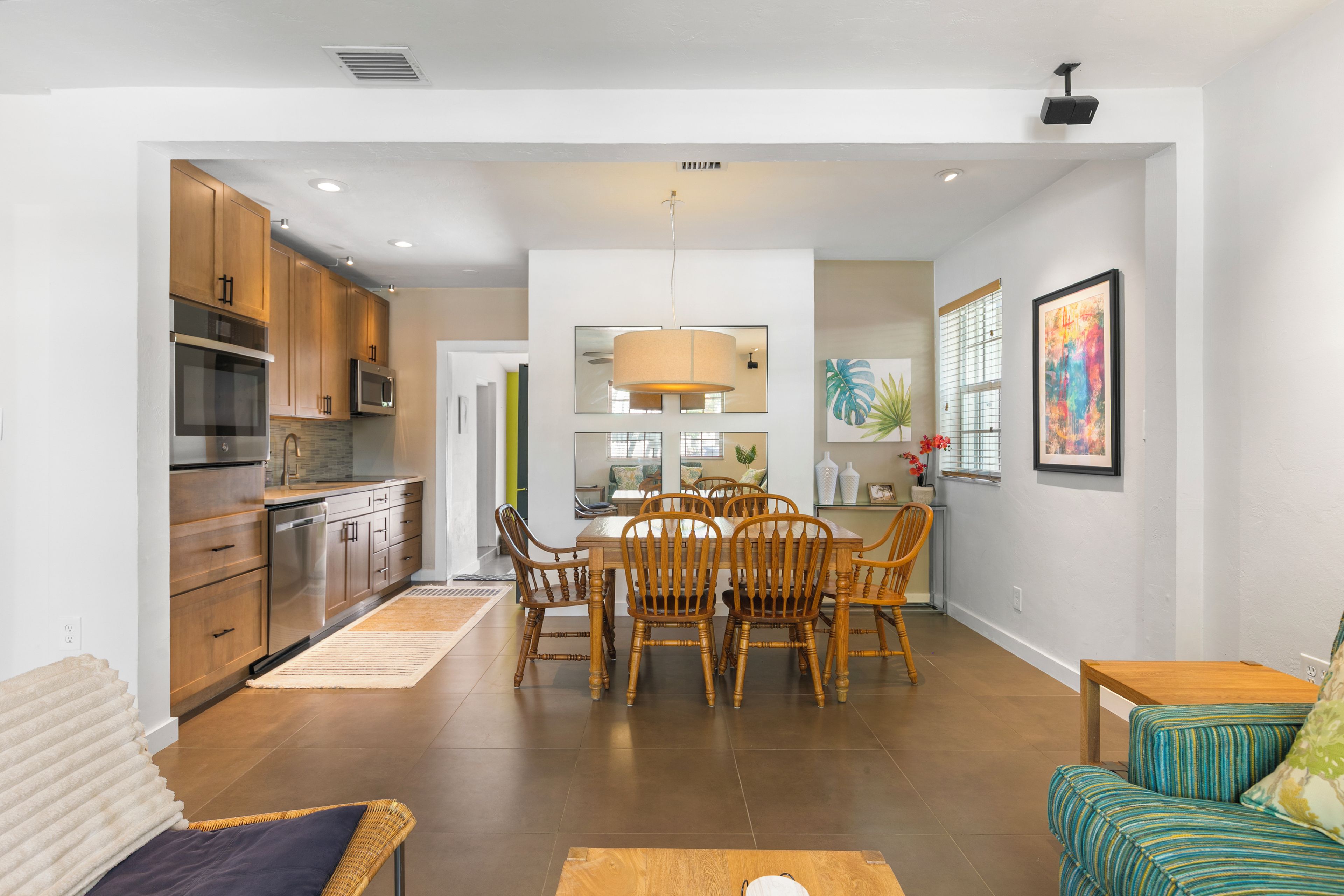 A modern kitchen with stainless steel appliances, a dining area with wooden chairs, and a living room with a sofa and a coffee table.