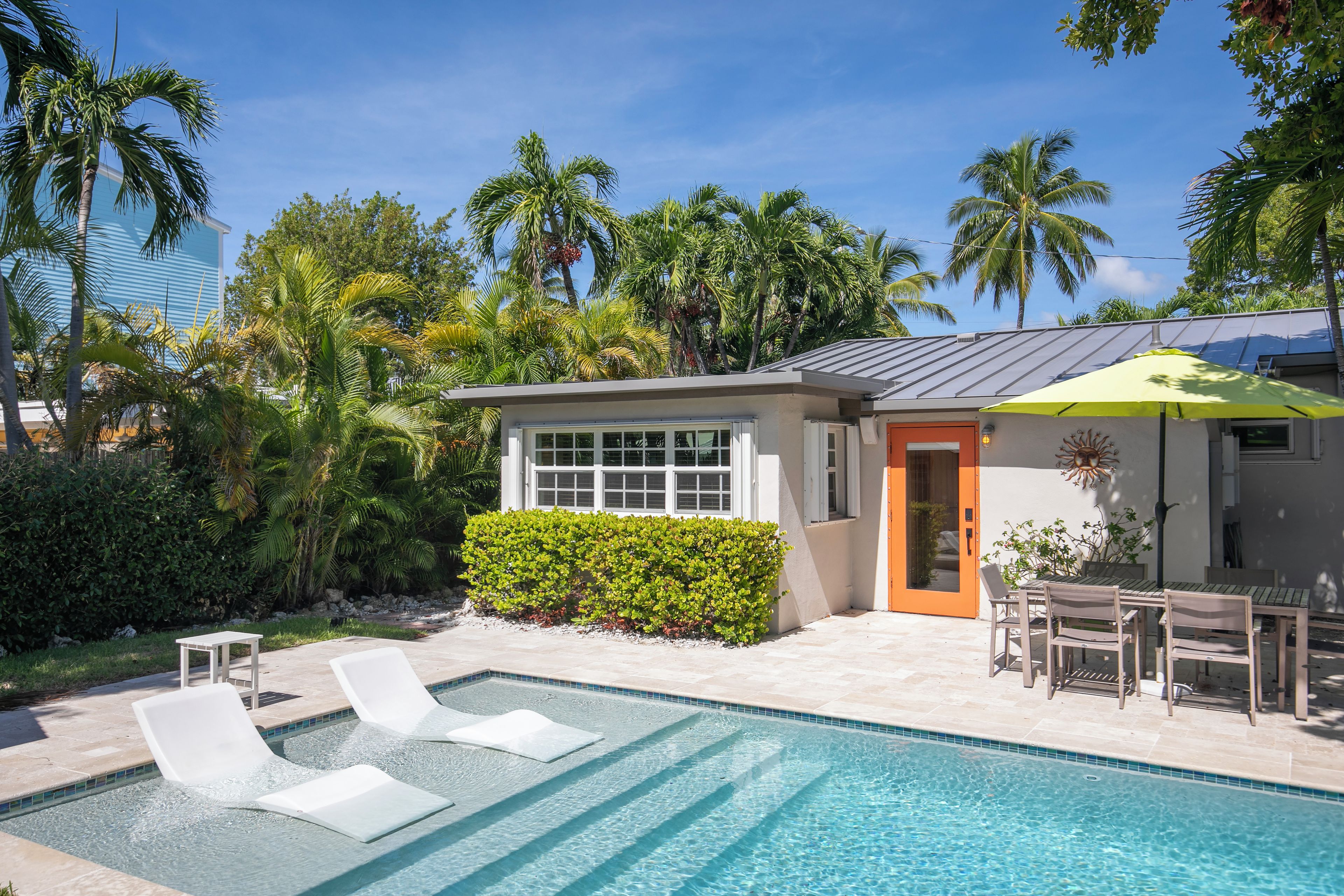 A swimming pool with lounge chairs, a small building with a door, and surrounding palm trees.