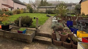 A residential backyard with a paved pathway, raised garden beds, and various plants. - Cozy vacation apartment in Aurach - peace, nature & comfort (Aurach)