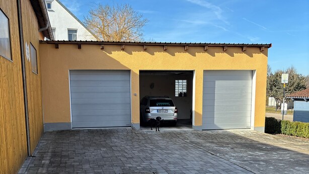 A building with two garage doors, a paved driveway, and a parked car. - Cozy vacation apartment in Aurach - peace, nature & comfort (Aurach)