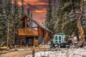 A log cabin with a balcony, a small attached shed, and a snow-covered landscape.
