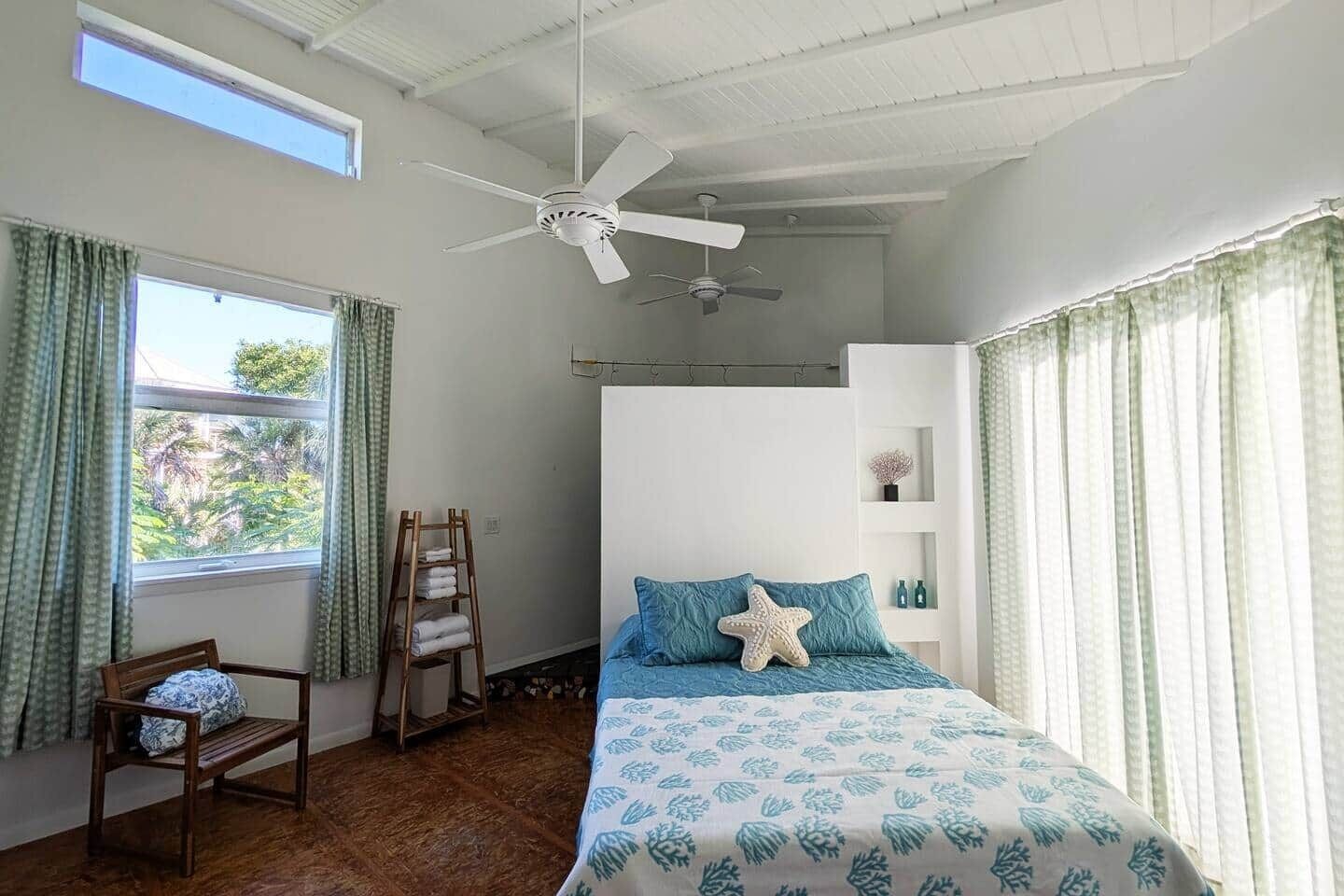 A bedroom with a bed, a chair, a ceiling fan, and a window with curtains.