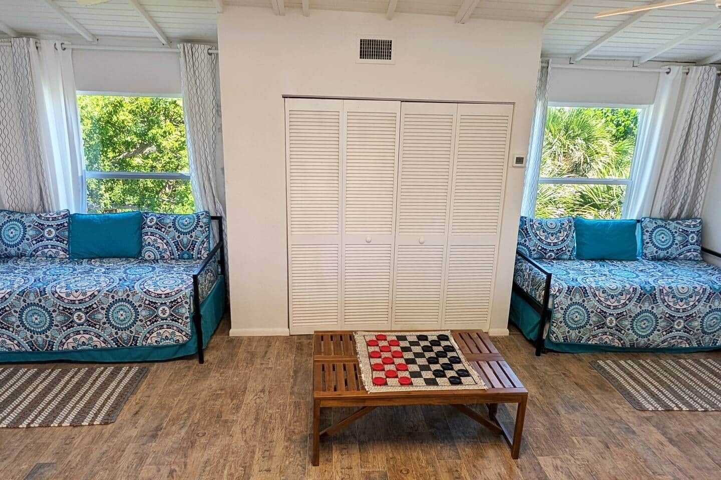 A room with two patterned sofas, a wooden coffee table with a checkered game, and a white closet with louvered doors.