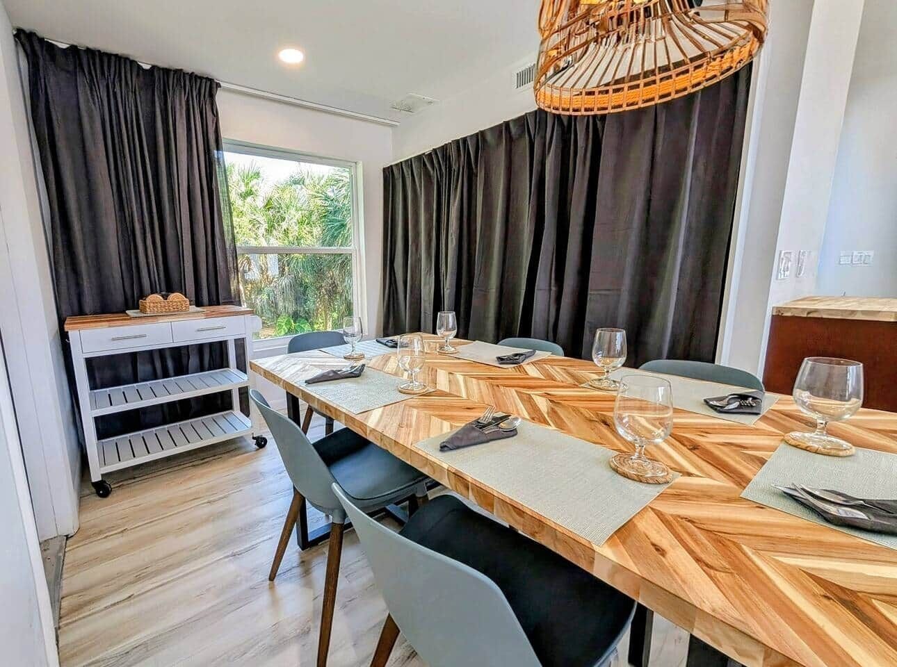 A dining area with a long wooden table, grey chairs, and a white cart with shelves.