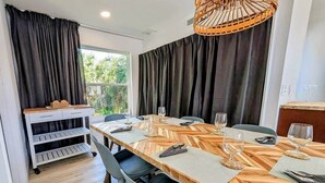 A dining area with a long wooden table, grey chairs, and a white cart with shelves.