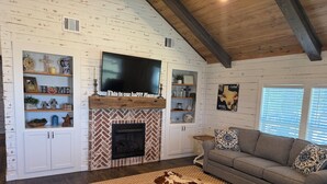 Una sala de estar acogedora con chimenea, un televisor montado encima y un sofá con cojines estampados.
