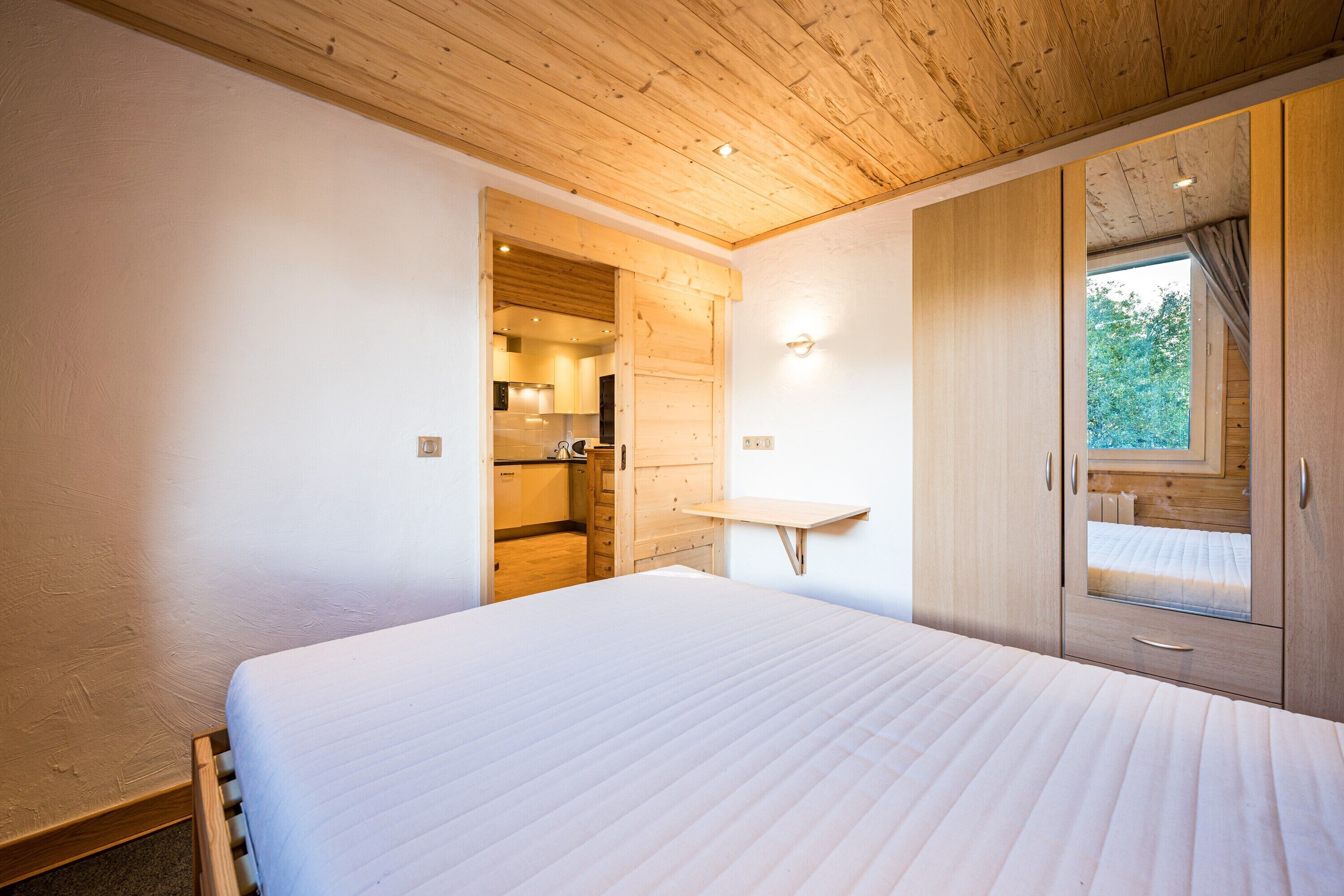 A bedroom with a wooden ceiling, a bed, a wardrobe, and a window.